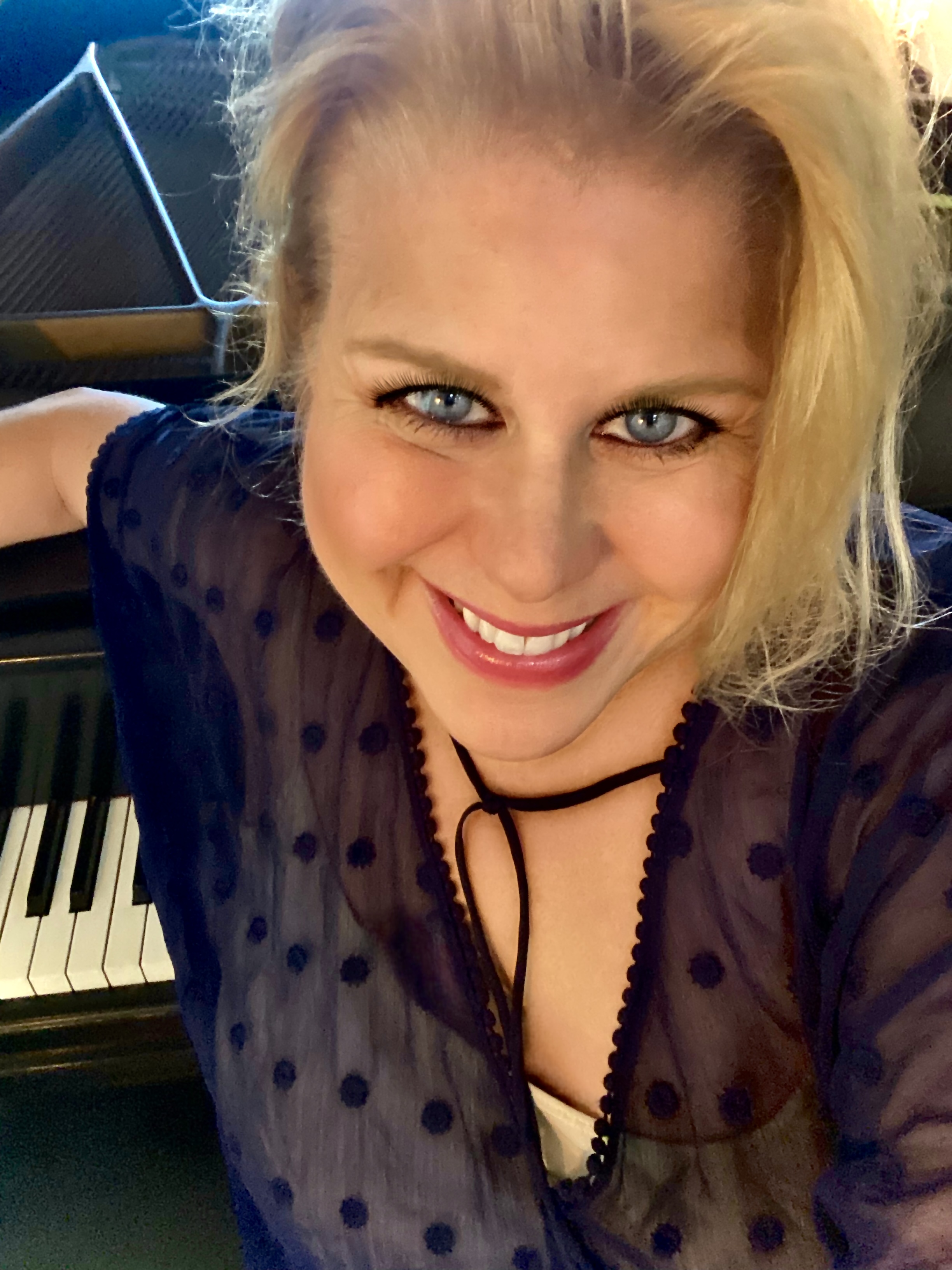 Dena Kay Jones, sitting in front of the piano, smiling directly at the camera.